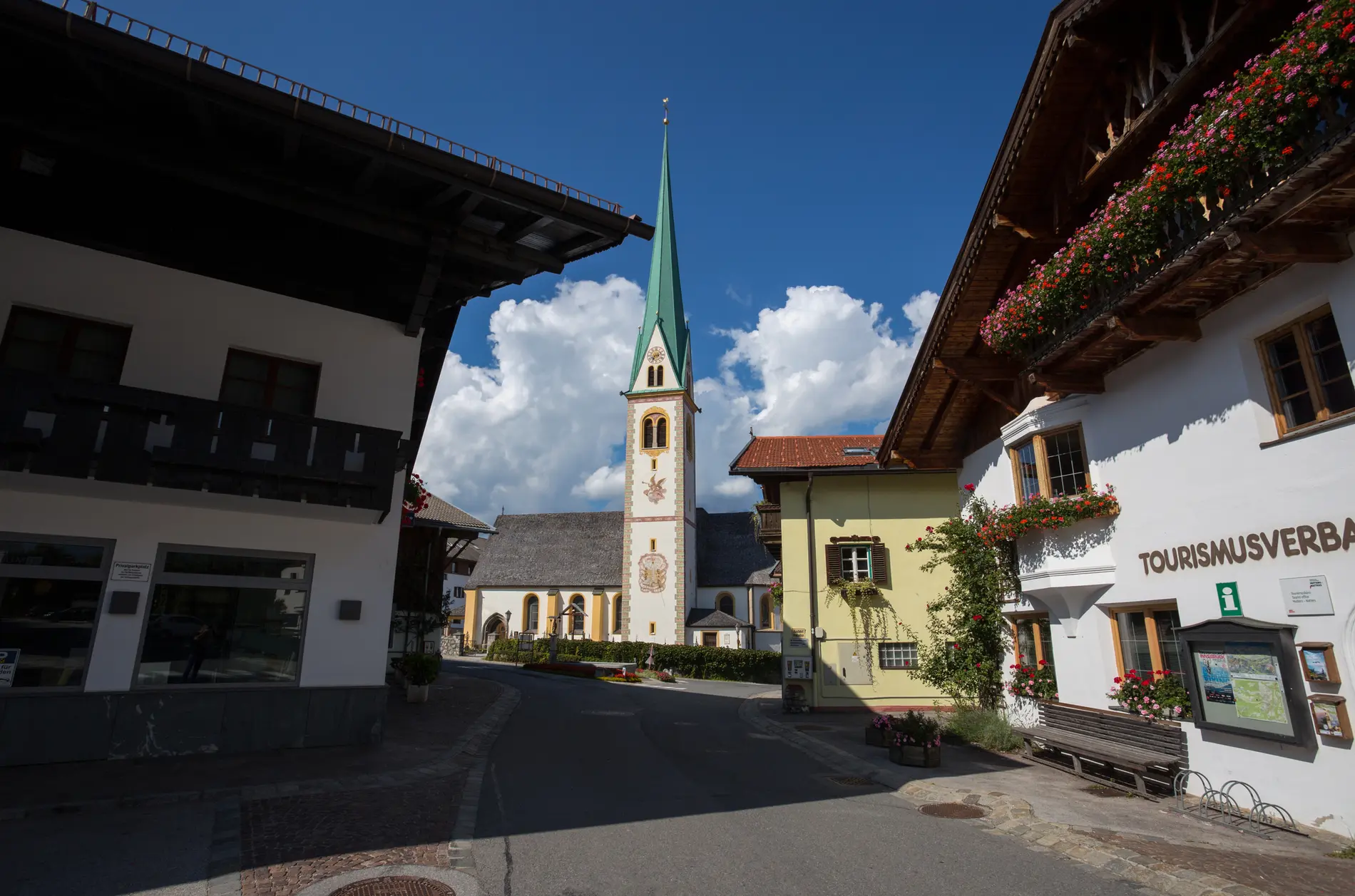 Vorplatz im Zentrum der Gemeinde Mutters in Tirol. Zu sehen ist eine Kirche, rechts der Tourismusverband. Alte Tirolerhäuser mit Holzbalkönen