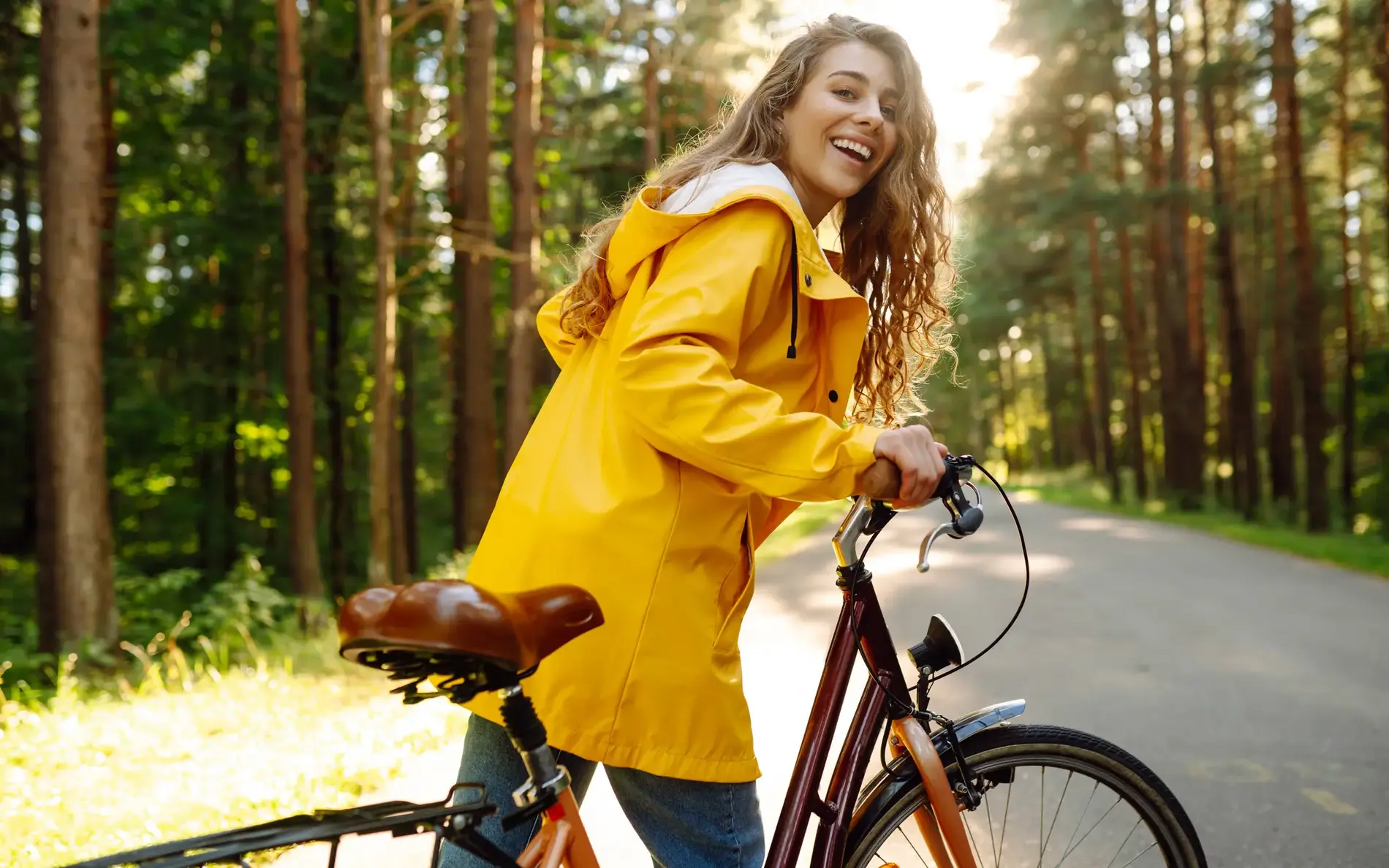 Frau mit gelber Jacke schiebt Fahrrad durch Waldgegend