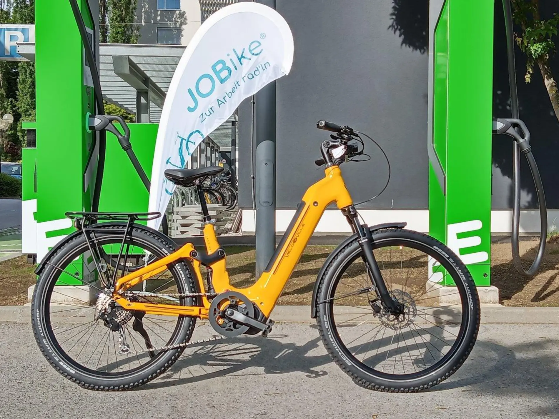 Ein E-Fahrrad, dahinter eine E-Ladesäule und eine Fahne mit der Aufschrift "JOBike"