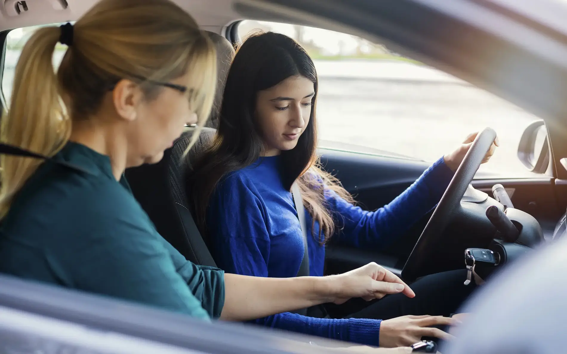 Fahrschülerin bekommt eine Einweisung ihrer Fahrlehrerin im Auto. Sie schauen auf die Gangschaltung.