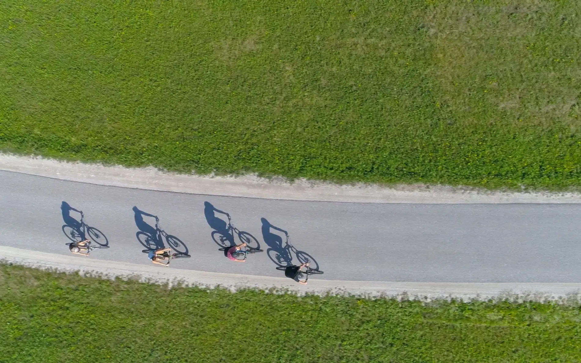 4 Radfahrer:innen von weit oben. Zu sehen sind die Schatten, die ihre Räder werfen.